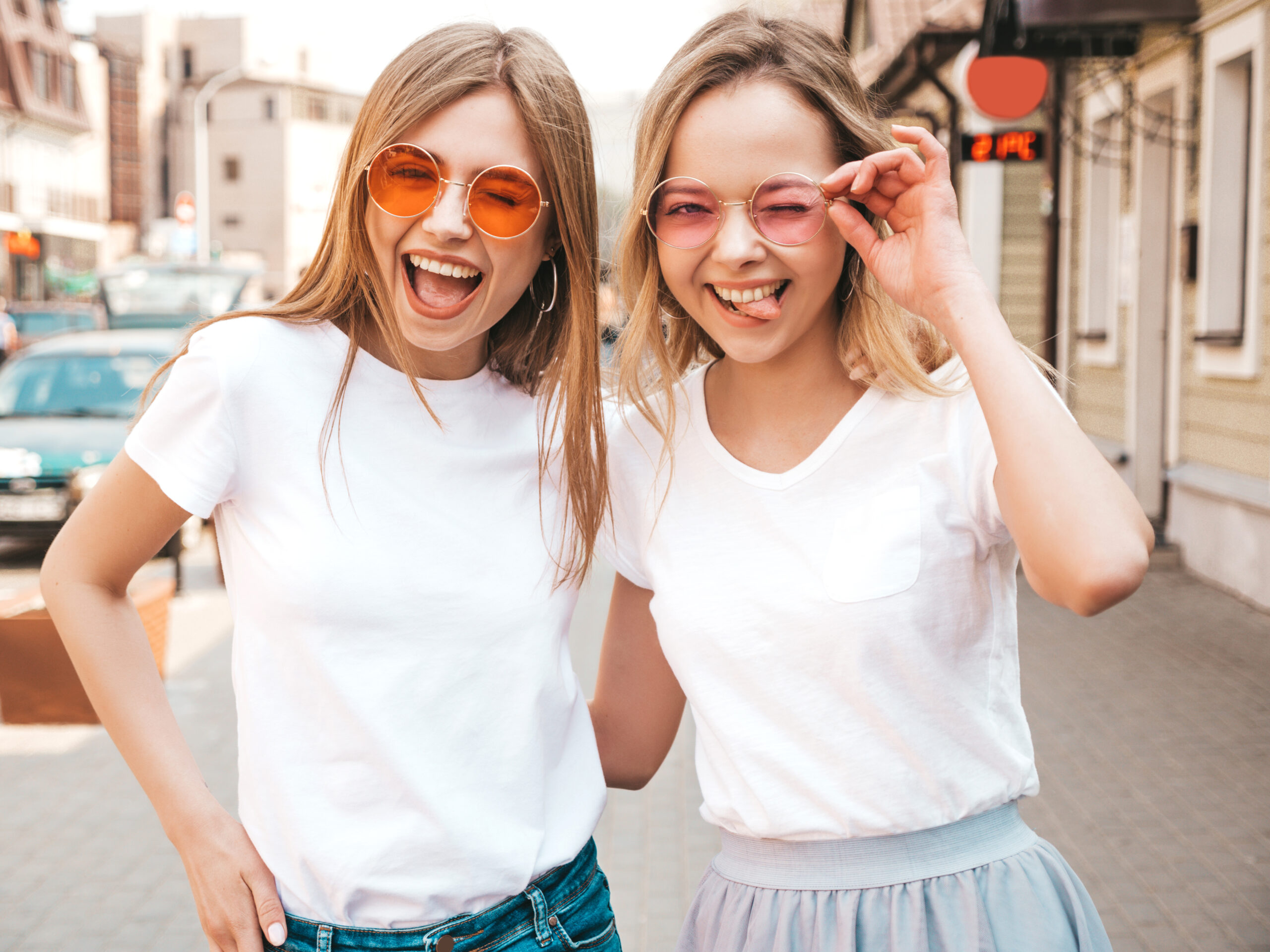 Portrait of two young beautiful blond smiling hipster girls in trendy summer white t-shirt clothes. Sexy carefree women posing on street background. Positive models having fun in sunglasses.Hugging